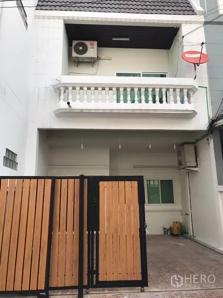 ทาวน์เฮาส์ ให้เช่าหรือขายในPhra Khanong, Bangkok - ด้านหน้าทาวน์เฮ้าส์หลายชั้นสีขาว พร้อมระเบียงและโรงจอดรถมีกำแพงรั้ว