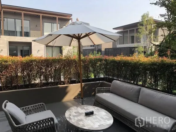 独立式住宅 出售在Bang Kapi, Bangkok - 私家露台配遮阳伞与藤编座椅，修剪整齐的绿篱与现代邻里景观。