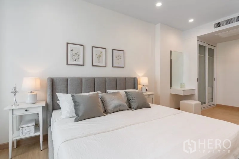Condominium for sale in Yan Nawa, Bangkok - Serene bedroom with upholstered headboard, bedside tables and a built-in wardrobe with dressing table.