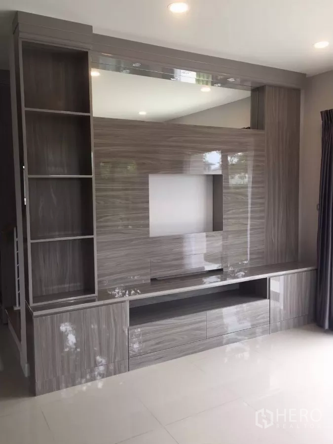 Detached House for rent in Samut Prakan - Built-in TV wall and shelving unit in the living area with spotlights.