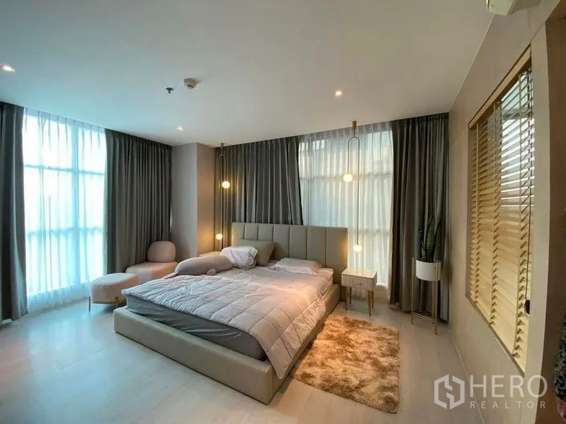 公寓 出售在Huai Khwang, Bangkok - 宽敞主卧，特大床、床侧吊灯、通高窗帘与角落休闲椅。