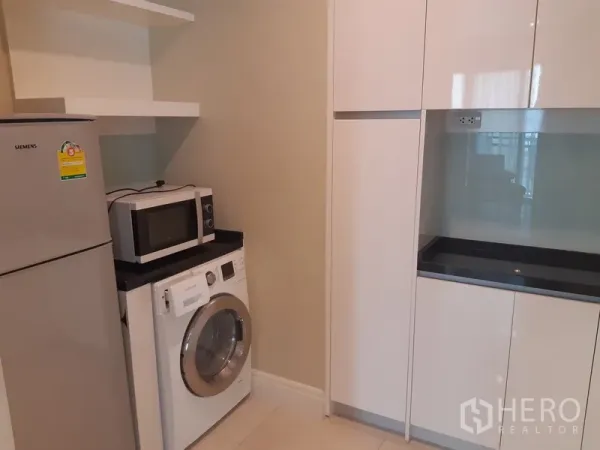 公寓 出租在Khlong Toei, Bangkok - 现代厨房，白色橱柜、黑色台面，冰箱、微波炉和前置洗衣机