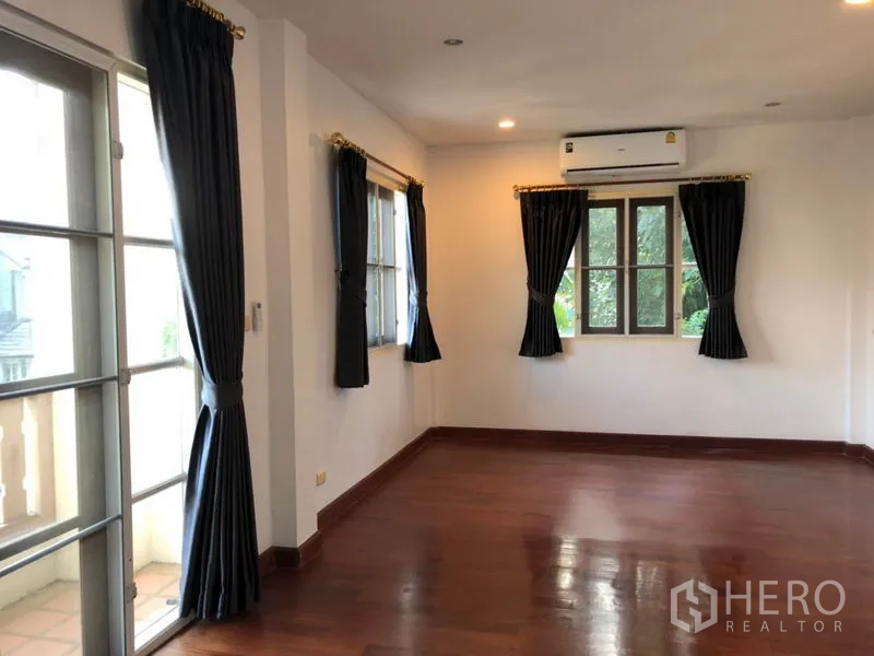 Detached House for rent in Saphan Sung, Bangkok - Upstairs bedroom with hardwood floors, dark curtains, balcony doors and air conditioning.