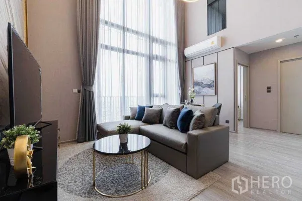 公寓 出租在Phra Khanong, Bangkok - 现代客厅，灰色沙发、圆形玻璃茶几、电视柜与通高窗帘。