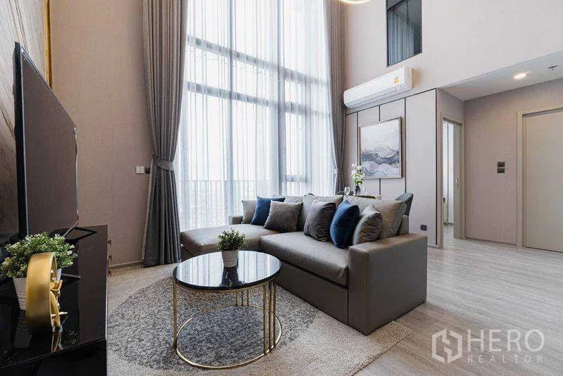 公寓 出租在Phra Khanong, Bangkok - 现代客厅，灰色沙发、圆形玻璃茶几、电视柜与通高窗帘。
