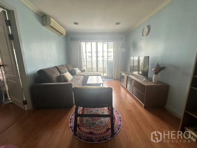 Condominium for rent in Watthana, Bangkok - Cozy living room with L-shaped sofa, TV console, wood floors and sliding doors to the balcony.