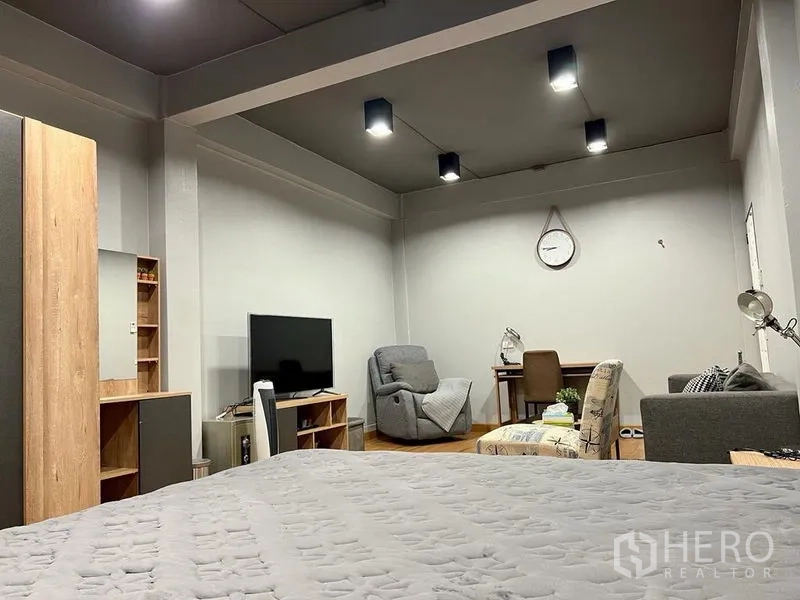 Shophouse for sale in Bang Kho Laem, Bangkok - Bedroom view toward TV, recliner and study desk under ceiling lights.