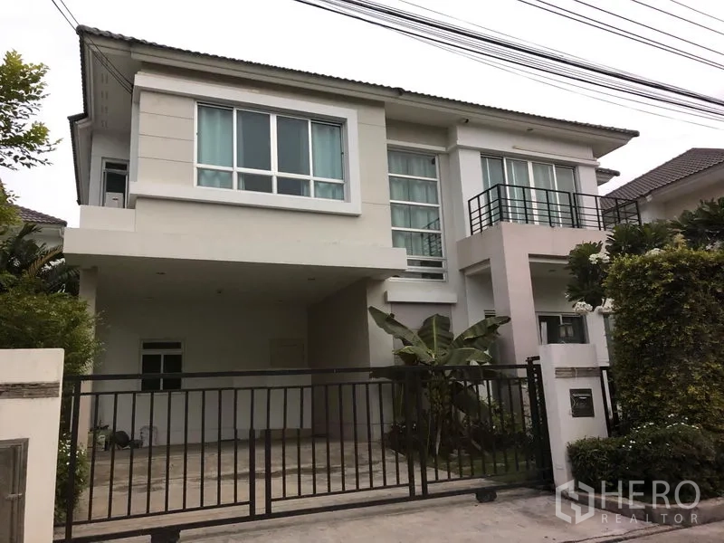 Detached House for sale in Saphan Sung, Bangkok - Modern two-storey detached house with large windows, small balcony, gated driveway and covered carport surrounded by greenery in Saphan Sung.