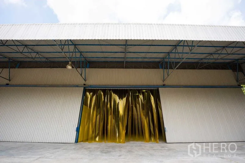 Warehouse for rent in Phra Phutthabat, Saraburi - Wide steel warehouse facade with sliding doors and yellow PVC strip curtain entrance.