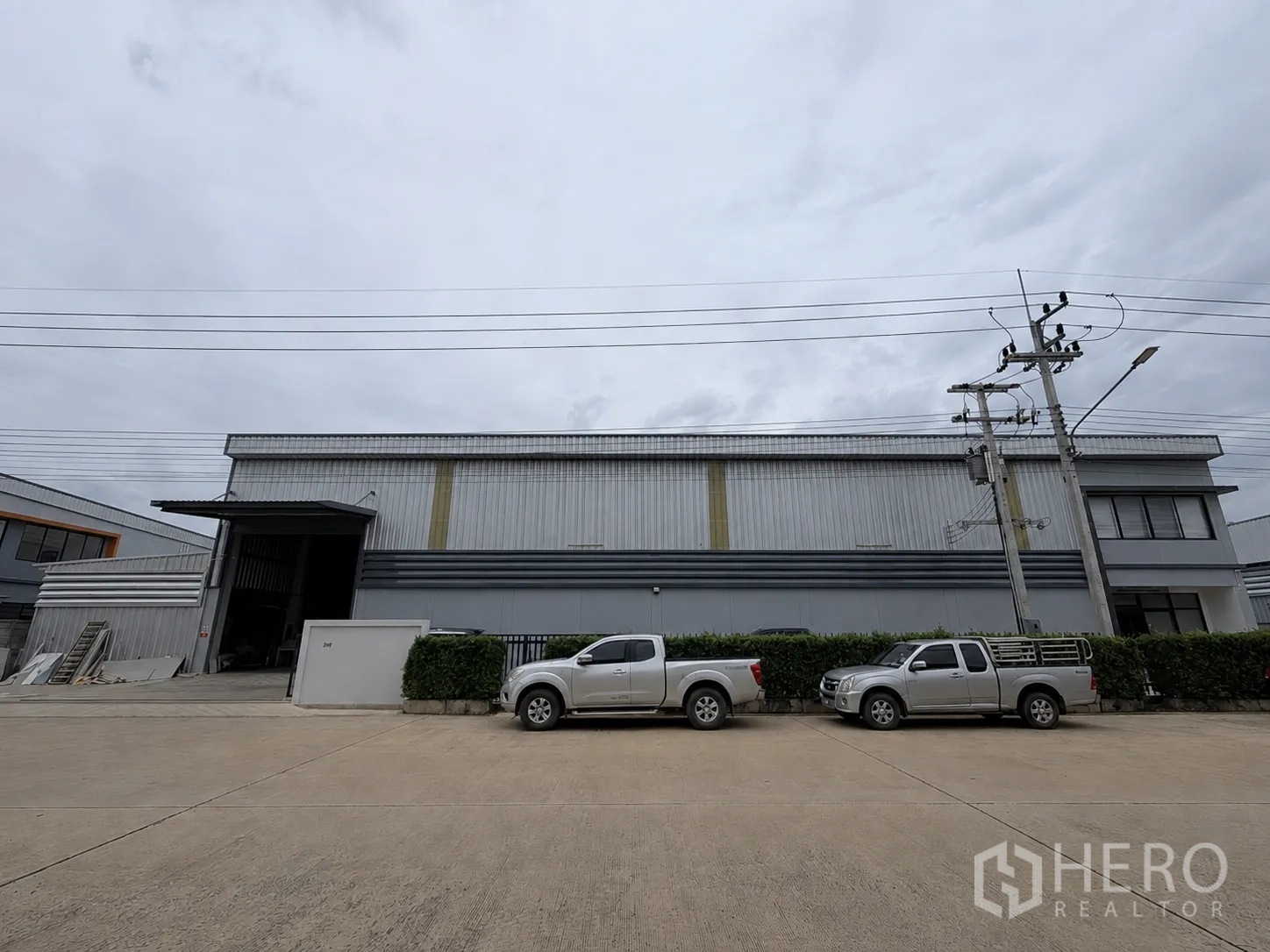โรงงาน for rent or sale in Lam Luk Ka, Pathum Thani - ด้านหน้าคลังสินค้าเมทัลชีทขนาดใหญ่มีรถกระบะจอดอยู่.