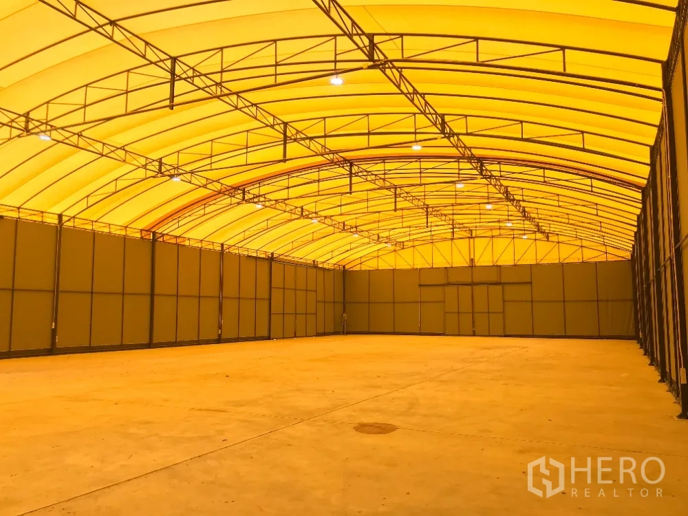 Warehouse for rent in Huai Khwang, Bangkok - Open warehouse interior with steel truss arched roof, ceiling lights, and smooth concrete floor.