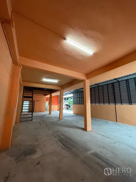 Warehouse for rent in Din Daeng, Bangkok - Spacious ground floor of the warehouse with fluorescent lighting, steel staircase to mezzanine and ventilated side panels.