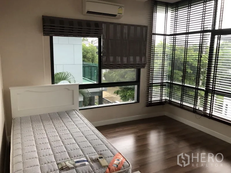 Detached House for rent in Bang Kapi, Bangkok - Corner bedroom with wraparound windows, blinds, and warm wood floors.