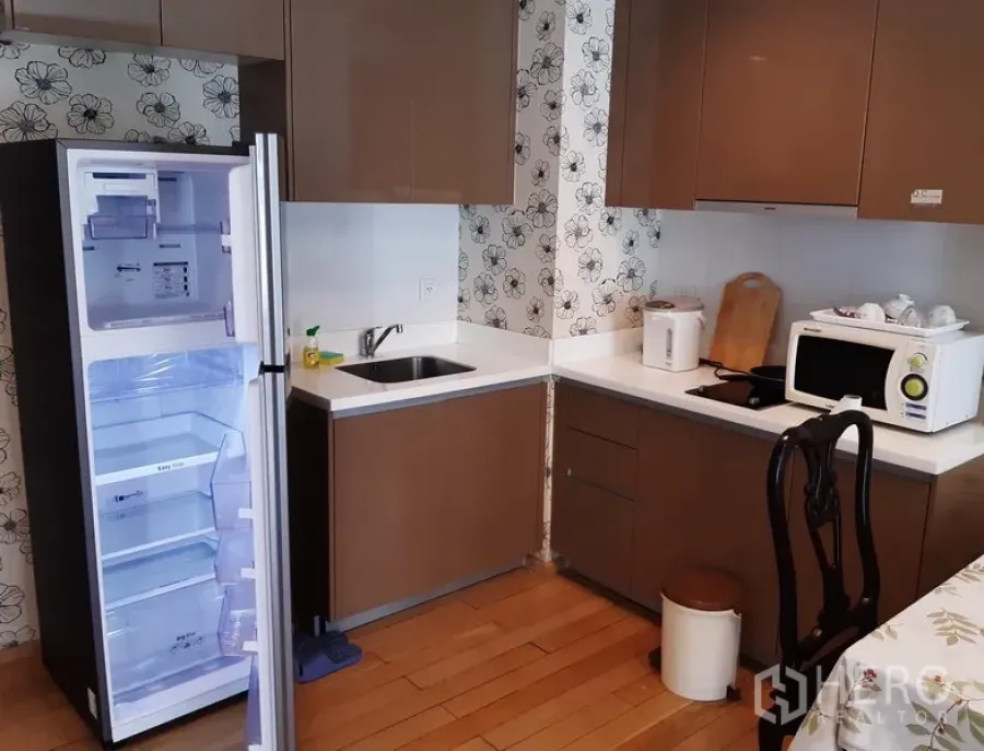 公寓 出租在Khlong Toei, Bangkok - 现代厨房，棕色柜体与白色台面，开启的冰箱、微波炉与电磁炉一应俱全。