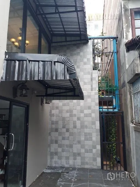 Townhouse for sale in Bang Kapi, Bangkok - Rear courtyard with tiled walls, glass door, and metal awnings with visible service pipes.