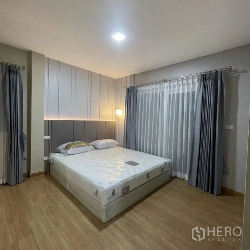 Semi-detached House for rent in Bang Phli, Samut Prakan - Spacious master bedroom with king bed, headboard lighting, wood flooring and floor-to-ceiling curtains.