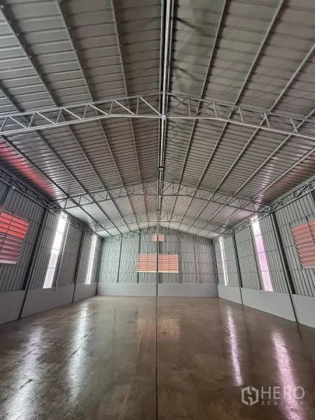 Warehouse for rent in Nonthaburi - Spacious warehouse interior with high steel roof, ventilation louvers and polished concrete floor.