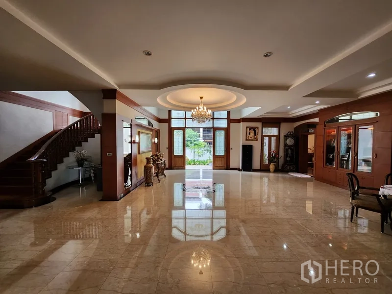 独立式住宅 出租在Prawet, Bangkok - 超大起居空间，水晶吊灯、高窗与弧形实木楼梯通往二层。