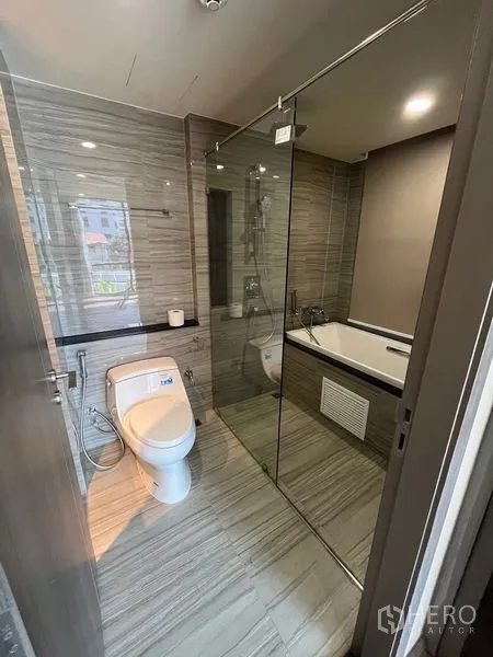 公寓 出租在Pathum Wan, Bangkok - 现代浴室，玻璃淋浴间、浴缸与坐便器，灰色石纹瓷砖。