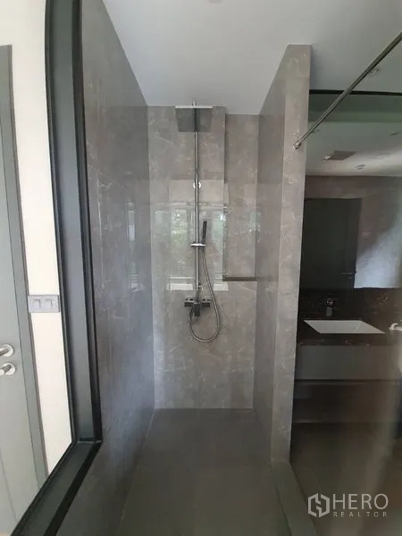 Condominium for sale in Huai Khwang, Bangkok - Ensuite shower with rain showerhead, gray marble-effect tiles and glass partition.