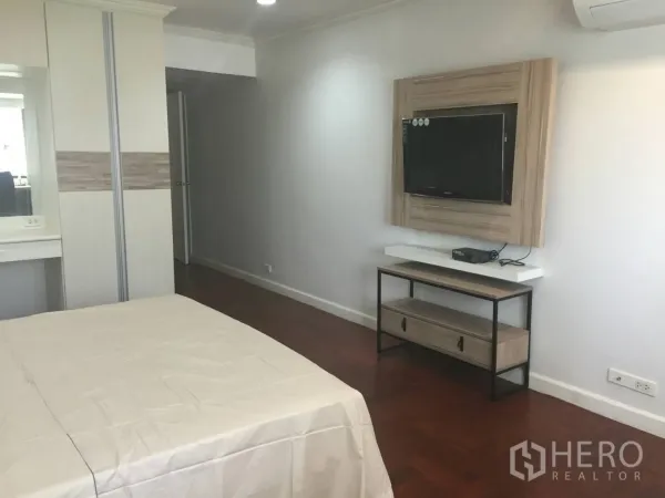 Condominium for rent in Watthana, Bangkok - Master bedroom with wall‑mounted TV, console, built‑in wardrobe and wood floors in a Watthana condo near BTS Phrom Phong.