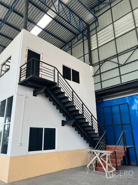 Warehouse for rent in Lat Krabang, Bangkok - Mezzanine office and black metal staircase under a high steel truss roof.
