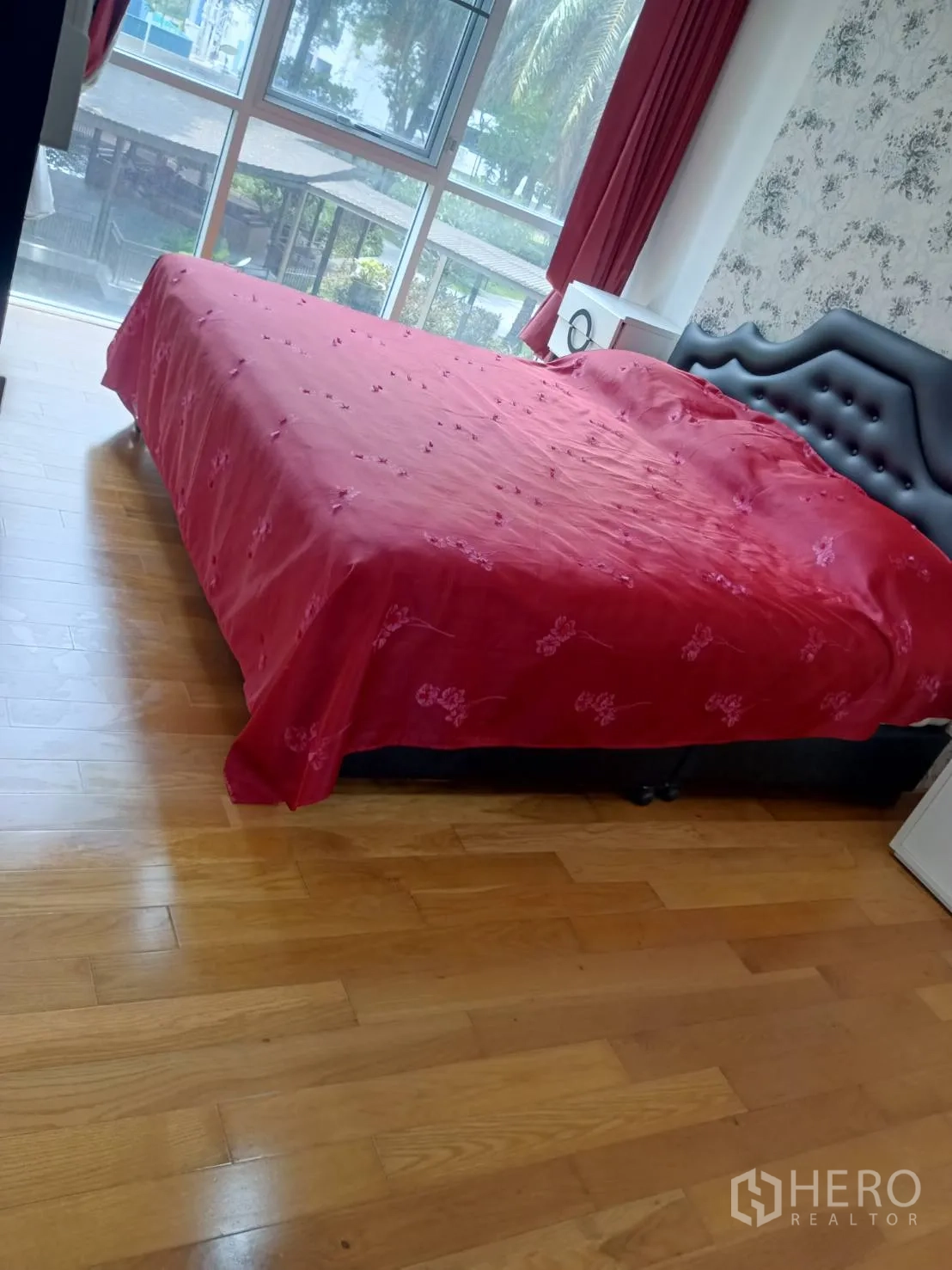 Condominium for sale in Chatuchak, Bangkok - Cozy bedroom with large window, red bedspread and garden view.