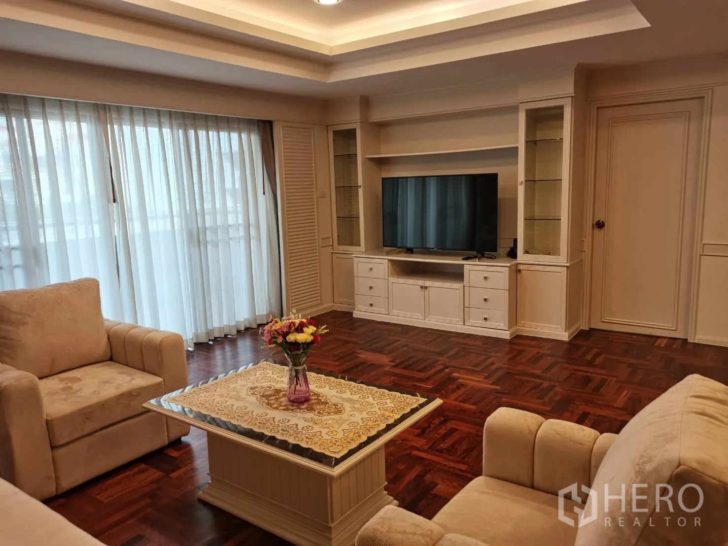 อพาร์ทเมนท์ ให้เช่าในWatthana, Bangkok - ห้องนั่งเล่นพร้อมชั้นบิวท์อินสำหรับทีวี โซฟาสีครีม ผ้าม่านโปร่ง และพื้นไม้เงางาม