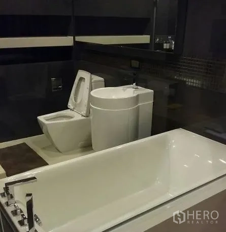 Condominium for rent in Sathon, Bangkok - Bathroom with white bathtub, pedestal sink, toilet and dark tile walls.