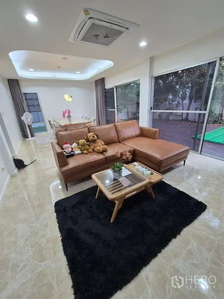 独立式住宅 出租在Bang Kruai, Nonthaburi - 客厅配L形皮沙发与落地玻璃，园景视野。