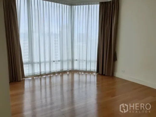 Condominium for rent in Watthana, Bangkok - Bright corner living area with floor-to-ceiling sheer curtains and warm wooden flooring in a high-rise Bangkok condo.