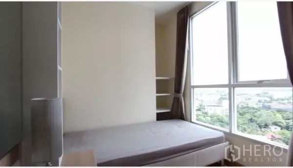 Condominium for rent in Watthana, Bangkok - Second bedroom with corner windows, shelving and green urban outlook.