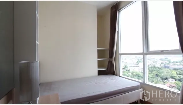 Condominium for rent in Watthana, Bangkok - Second bedroom with corner windows, shelving and green urban outlook.