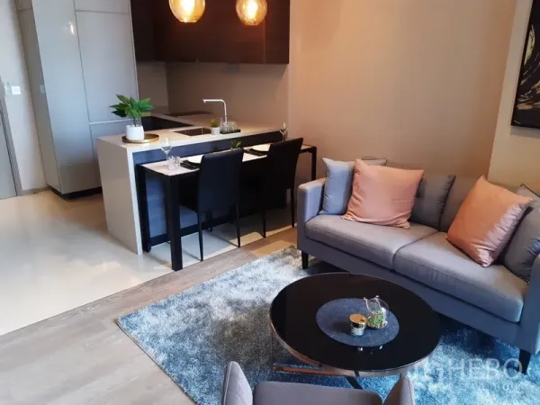 公寓 出租或出售在Watthana, Bangkok - 温馨客厅，灰色沙发、茶几与地毯，可望向厨房区域。