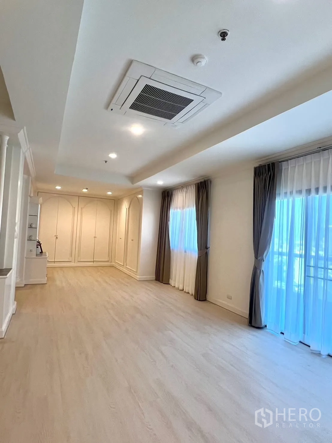 Condominium for rent in Khlong Toei, Bangkok - Large bedroom with wall closets, curtains and sliding doors to a balcony.