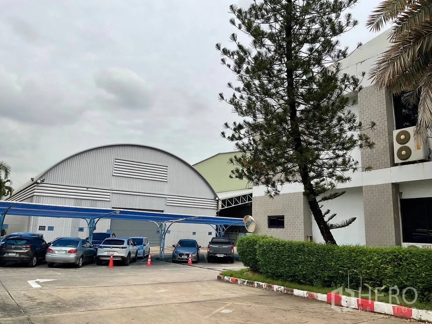 Warehouse for rent in Lak Si, Bangkok - Compound view showing the warehouse beside an office building with covered parking and landscaping.