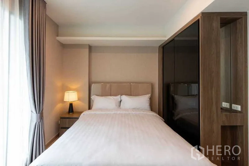 Condominium for rent in Huai Khwang, Bangkok - Bedroom with queen bed, bedside lamp and fitted wardrobe.