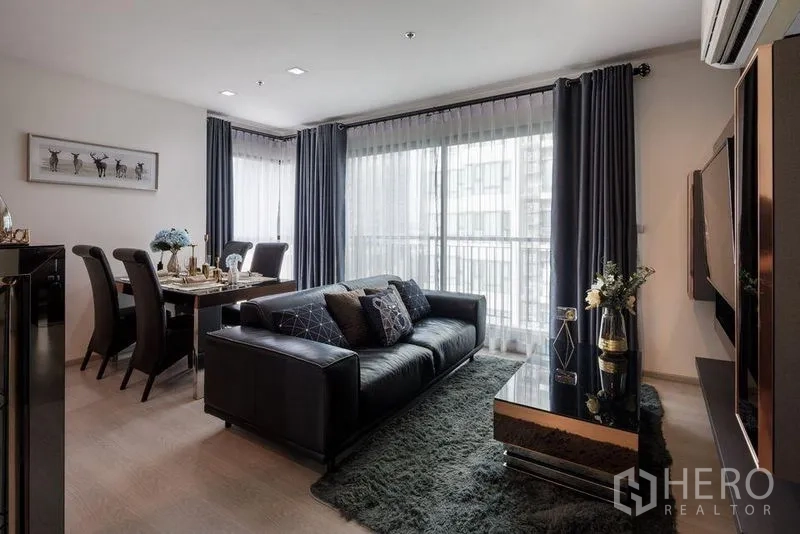 公寓 出租或出售在Khlong Toei, Bangkok - 明亮客厅，皮沙发，四人餐桌，带窗帘的阳台落地玻璃。