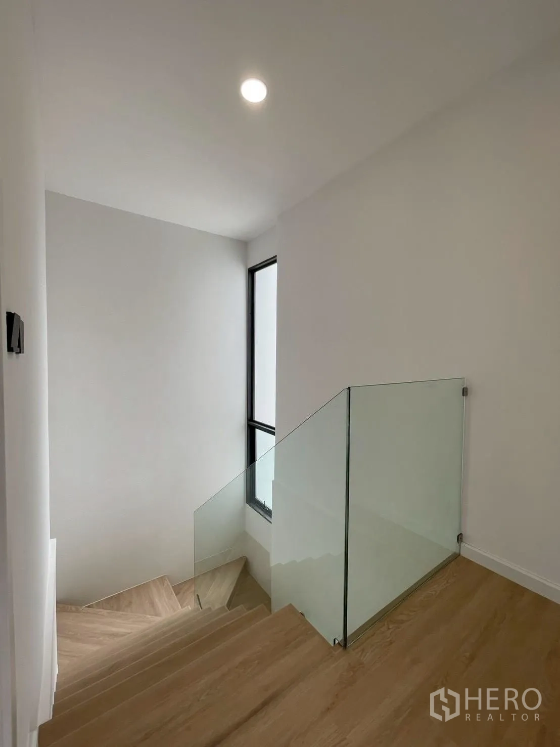 Detached House for sale in Chatuchak, Bangkok - Staircase with wooden steps and clear glass balustrade beside a tall window.