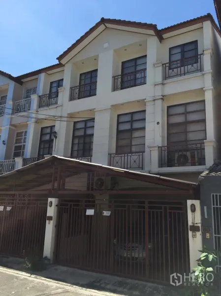 联排别墅 出售在Phra Khanong, Bangkok - 帕卡侬三层联排别墅外观，带阳台、坡屋顶与带门禁车棚，位于安静小巷