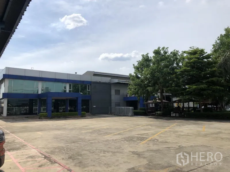 Factory for rent in Lam Luk Ka, Pathum Thani - Modern two‑storey office building with glass facade next to factory halls and parking area.