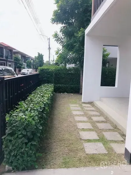 บ้าน ขายในSuan Luang, Bangkok - ทางเดินสวนหน้าบ้านแบบแผ่นทางเดิน ข้างรั้วสีดำและพุ่มไม้