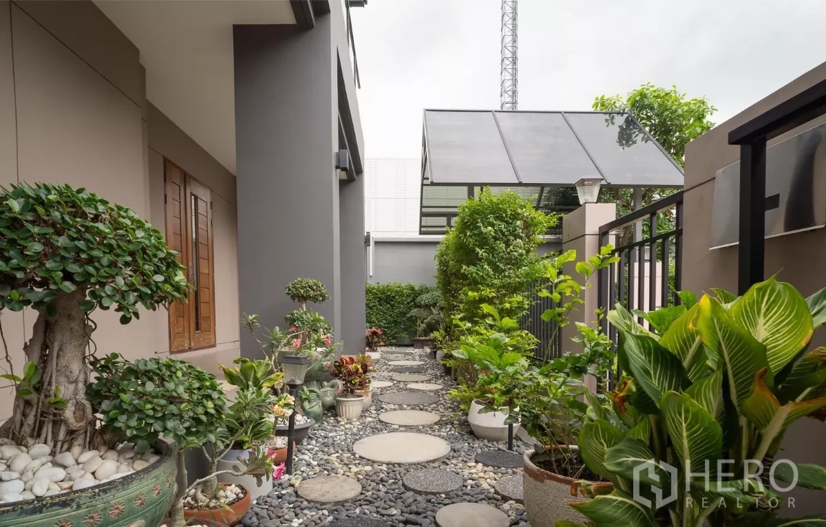 Detached House for rent or sale in Saphan Sung, Bangkok - Side garden with pebble stepping‑stone path lined with decorative potted plants.