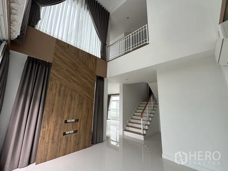 บ้าน ขายในLam Luk Ka, Pathum Thani - โถงรับแขกเพดานจั่วสูง พร้อมผ้าม่านยาวและผนังลายไม้