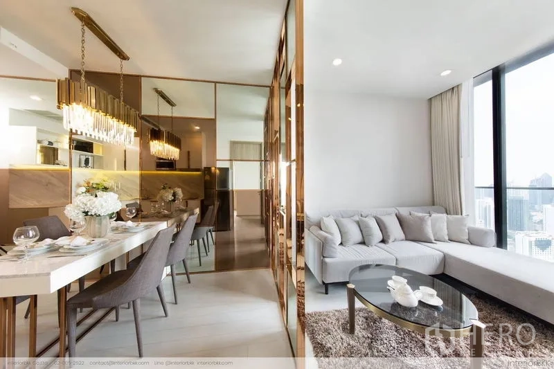 Condominium for rent in Pathum Wan, Bangkok - Open-plan dining and living with mirrored gold partition, sectional sofa and round coffee table.