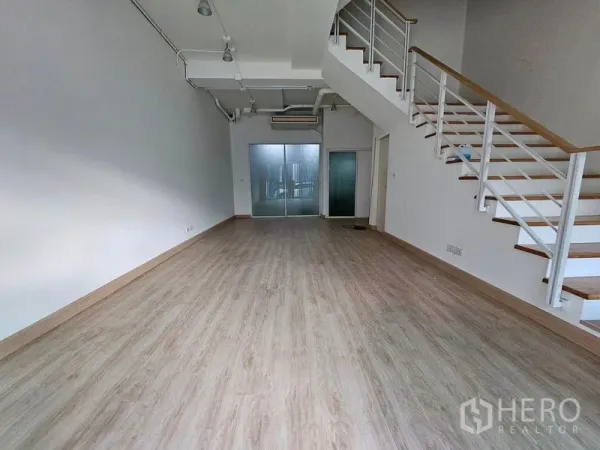 Townhouse for rent in Wang Thonglang, Bangkok - Open-plan living area with high ceiling, light wood floors, and a floating staircase leading upstairs.