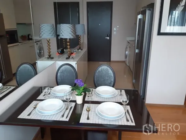 คอนโด ให้เช่าในWatthana, Bangkok - โต๊ะอาหาร 4 ที่นั่งจัดเซ็ตอยู่ข้างผนังกระจก มองเห็นประตูทางเข้าและมุมซักผ้า