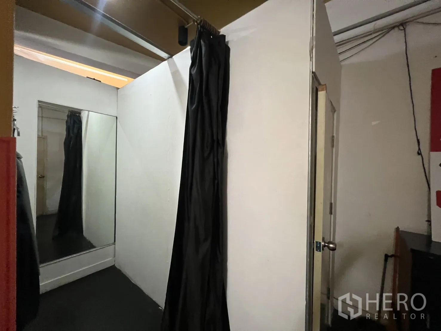 อาคารพาณิชย์ ให้เช่า - ห้องลองเสื้อภายในร้าน มีกระจกเต็มตัวและผ้าม่านสีดำ.