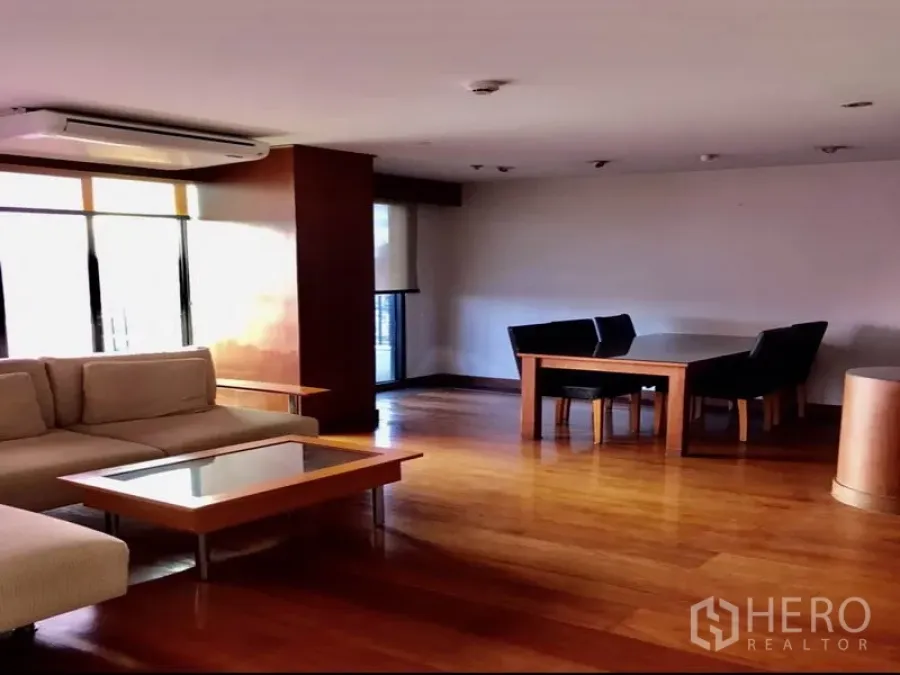 Condominium for rent or sale in Watthana, Bangkok - Spacious living and dining area with hardwood floors, L-shaped sofa and large windows.