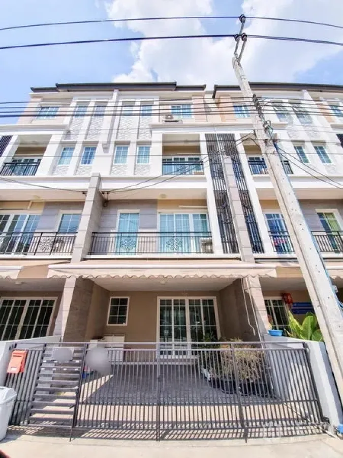 联排别墅 出租在Bang Na, Bangkok - 现代多层联排别墅立面，设阳台与推拉门，前方为带门庭院车位。